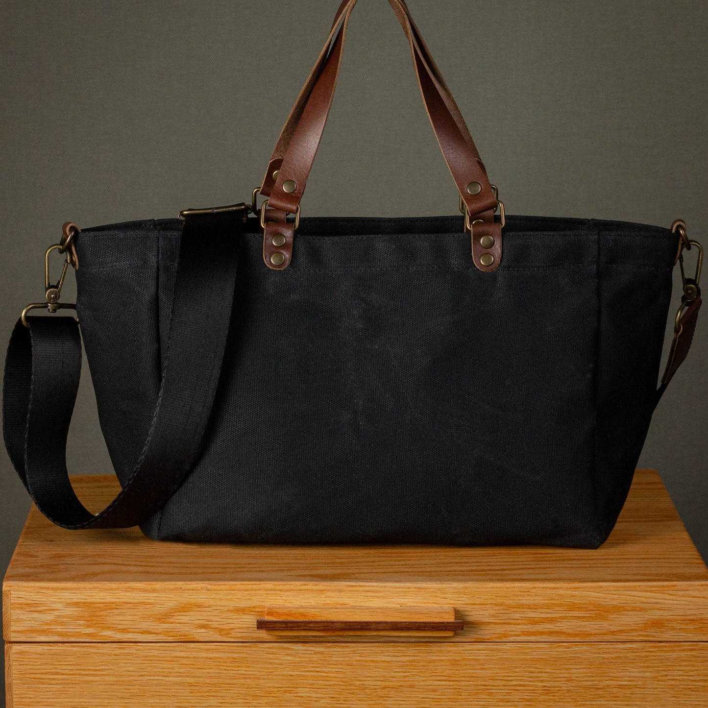 Black bag with brown straps on a wooden surface against a gray background