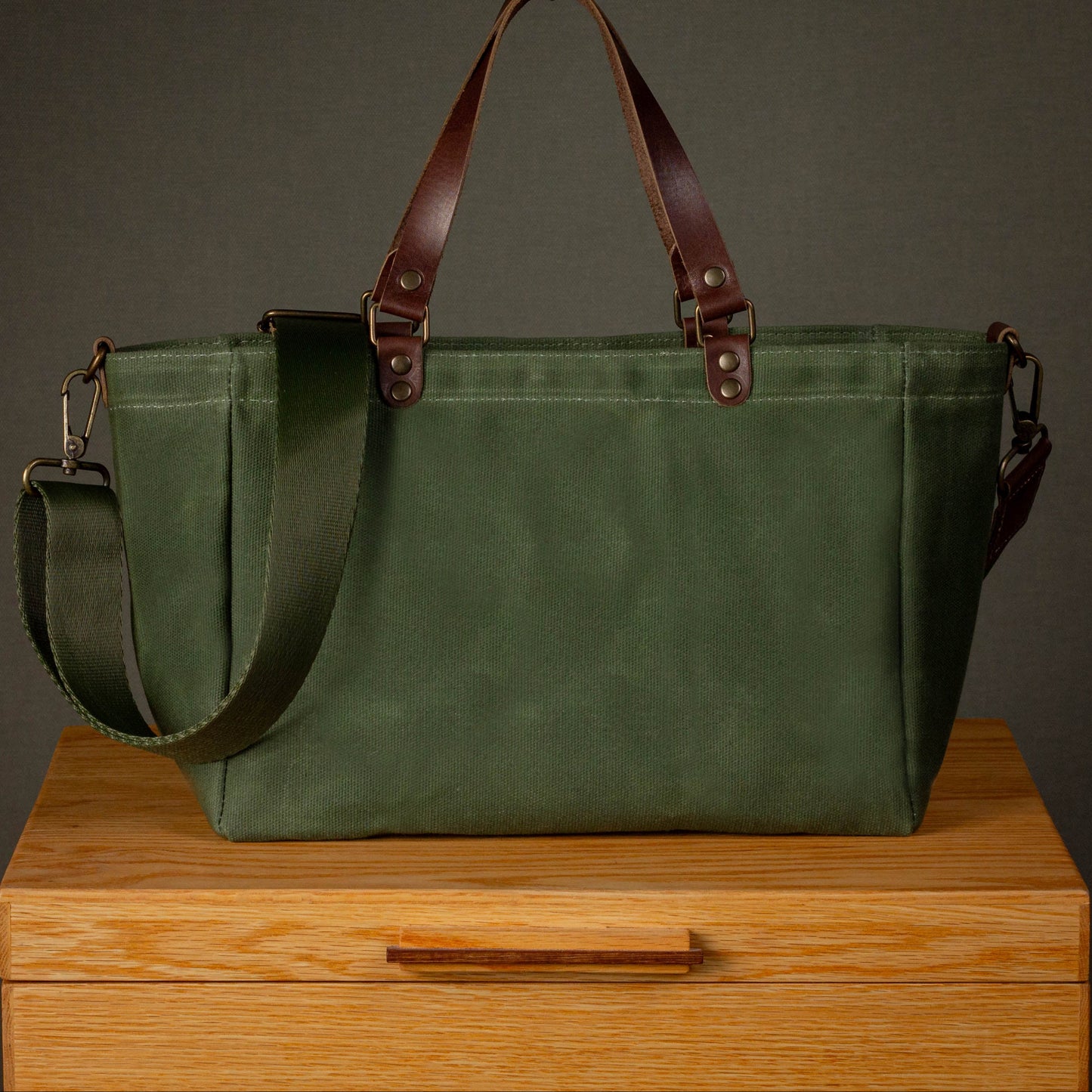 Green canvas bag with brown leather straps on a wooden surface