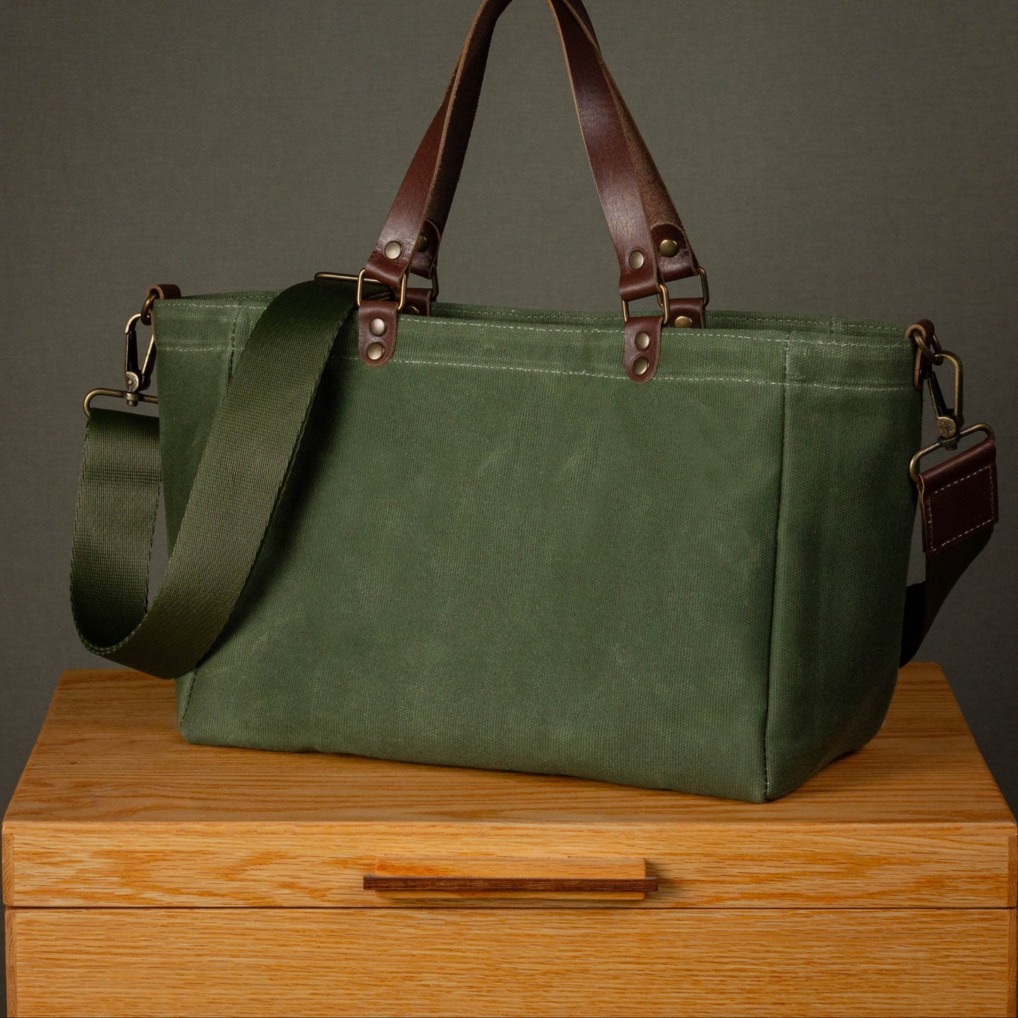 Green bag with brown straps on a wooden surface against a gray background
