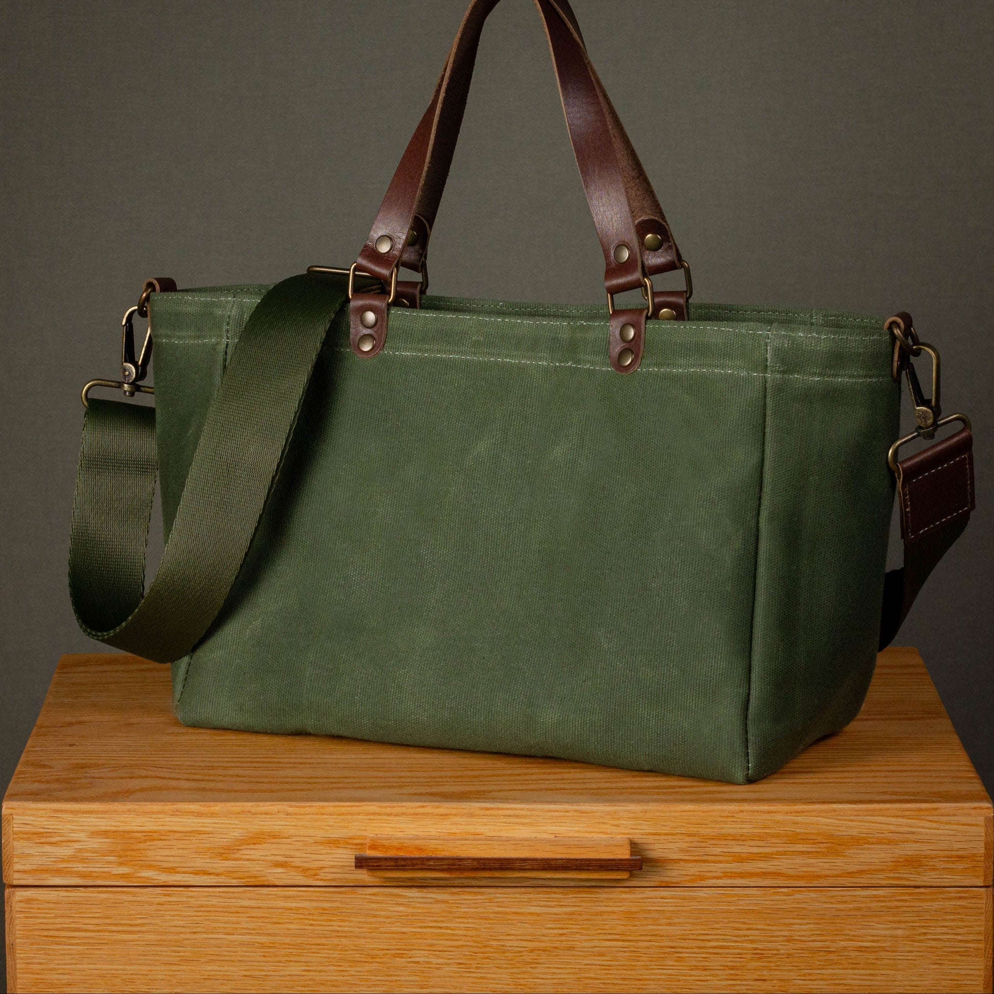 Green bag with brown straps on a wooden surface against a gray background