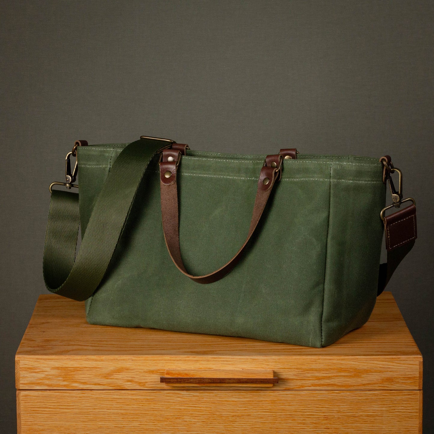 Green leather bag with brown straps on a wooden surface against a gray background