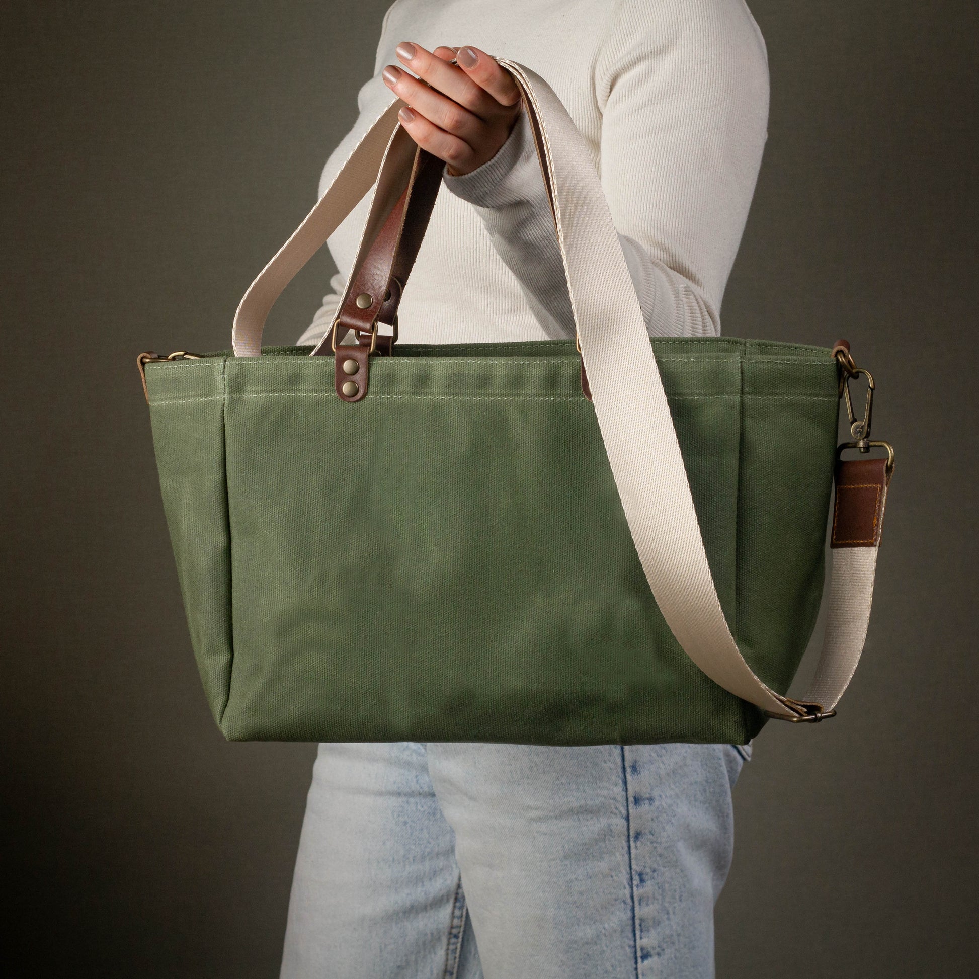 Green tote bag with brown straps held by a person against a dark background
