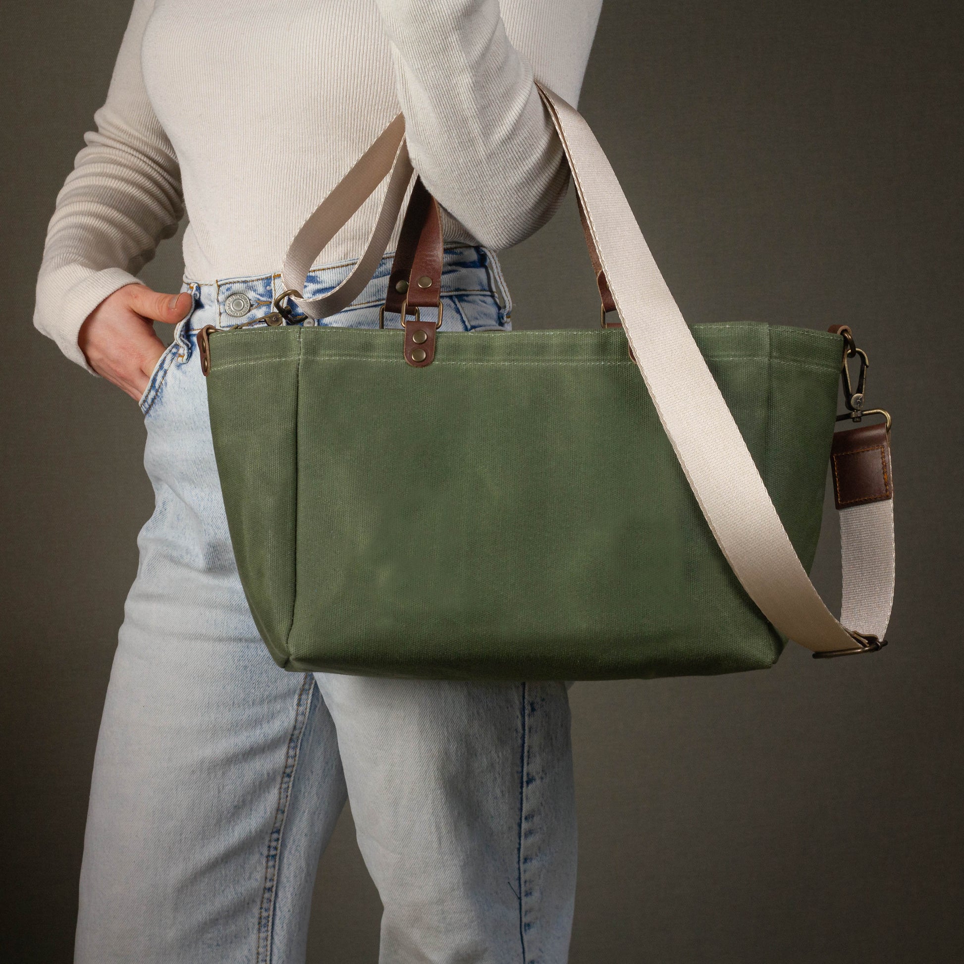 Person holding a green bag with a brown strap against a dark background