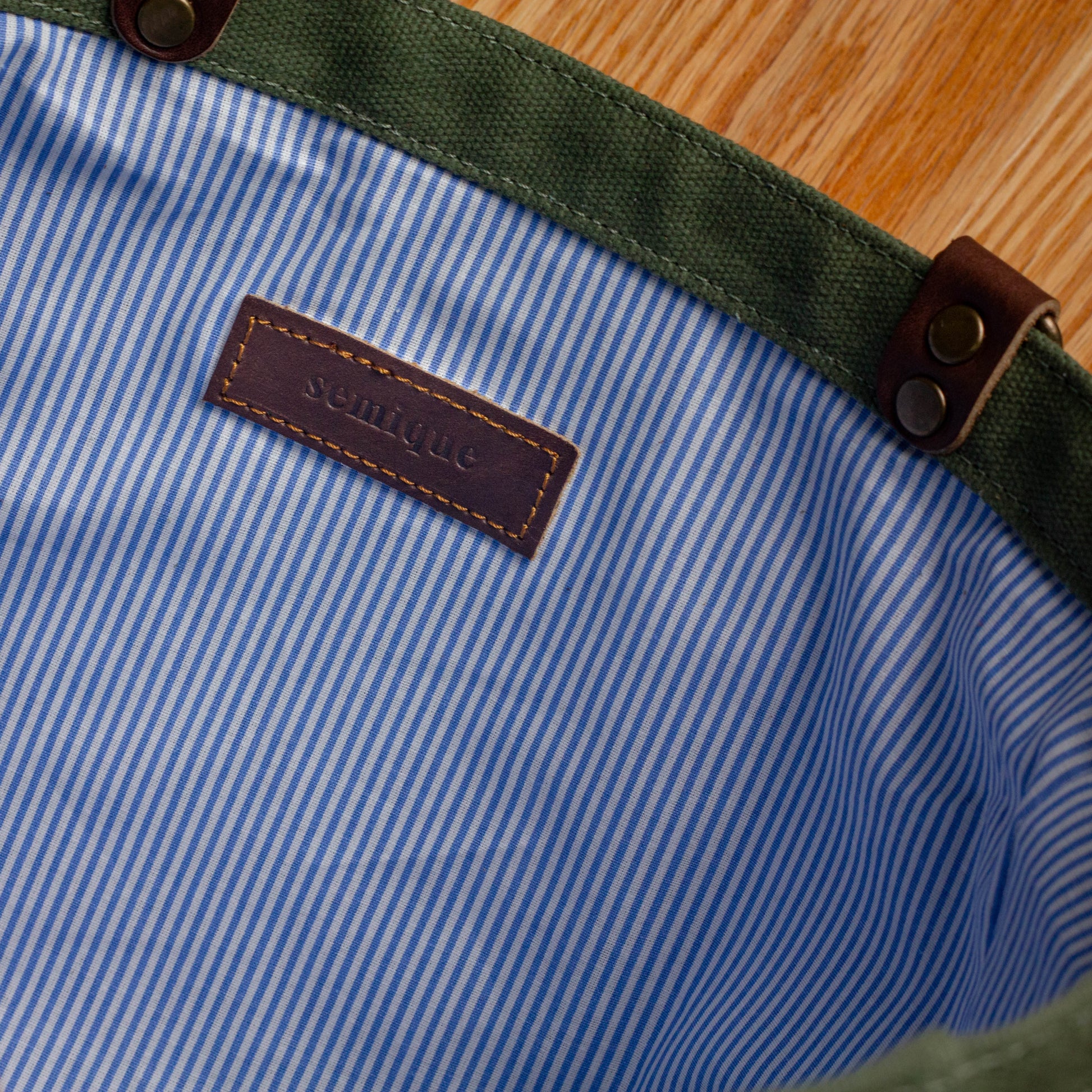 Close-up of a blue and white striped fabric with a green border and brown leather label on a wooden surface.