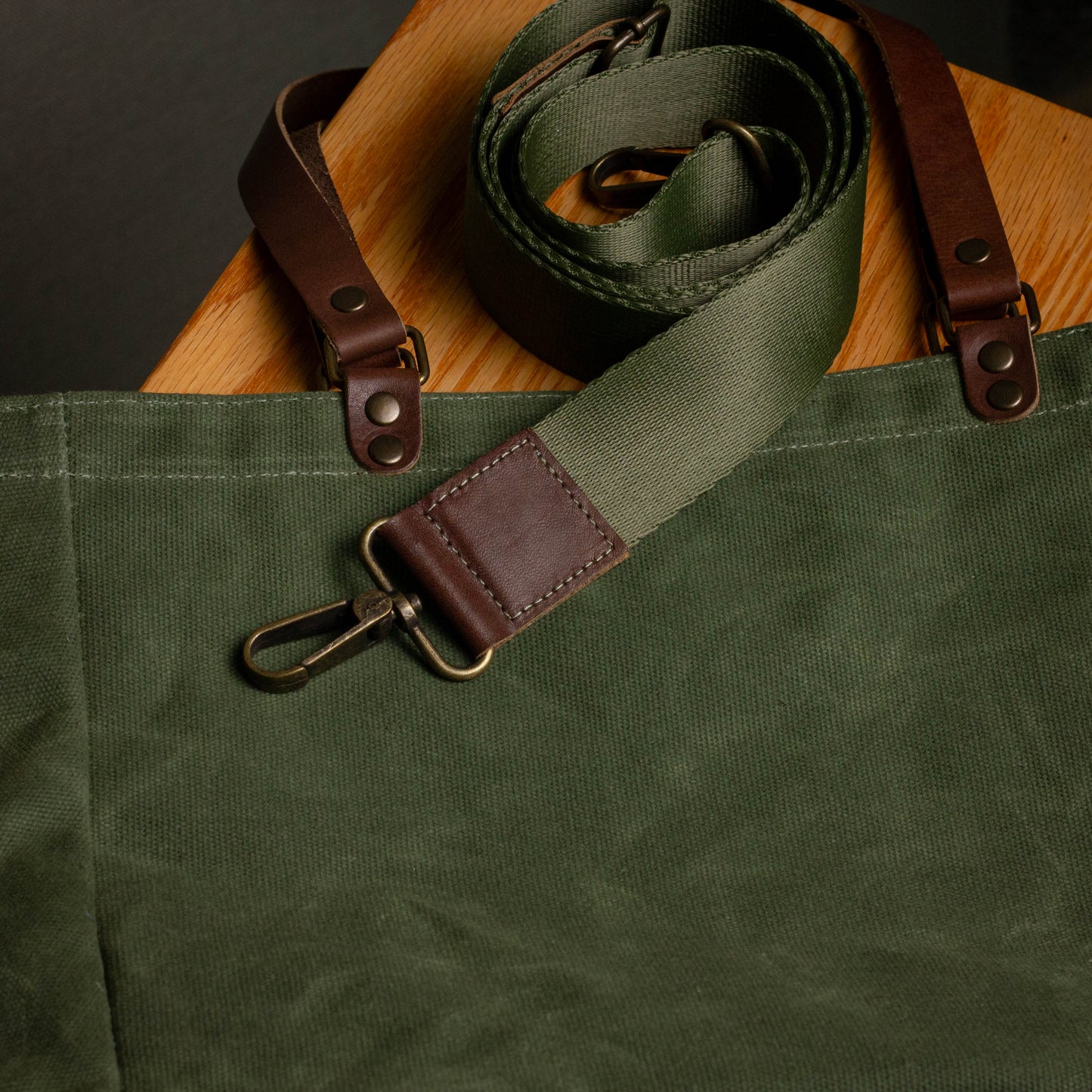 Green waxed canvas bag with brown leather strap on a wooden surface