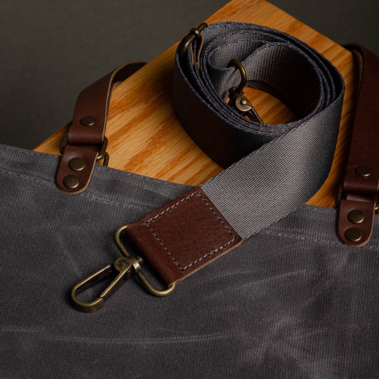 Gray strap with brown leather ends on a gray bag against a wooden surface.
