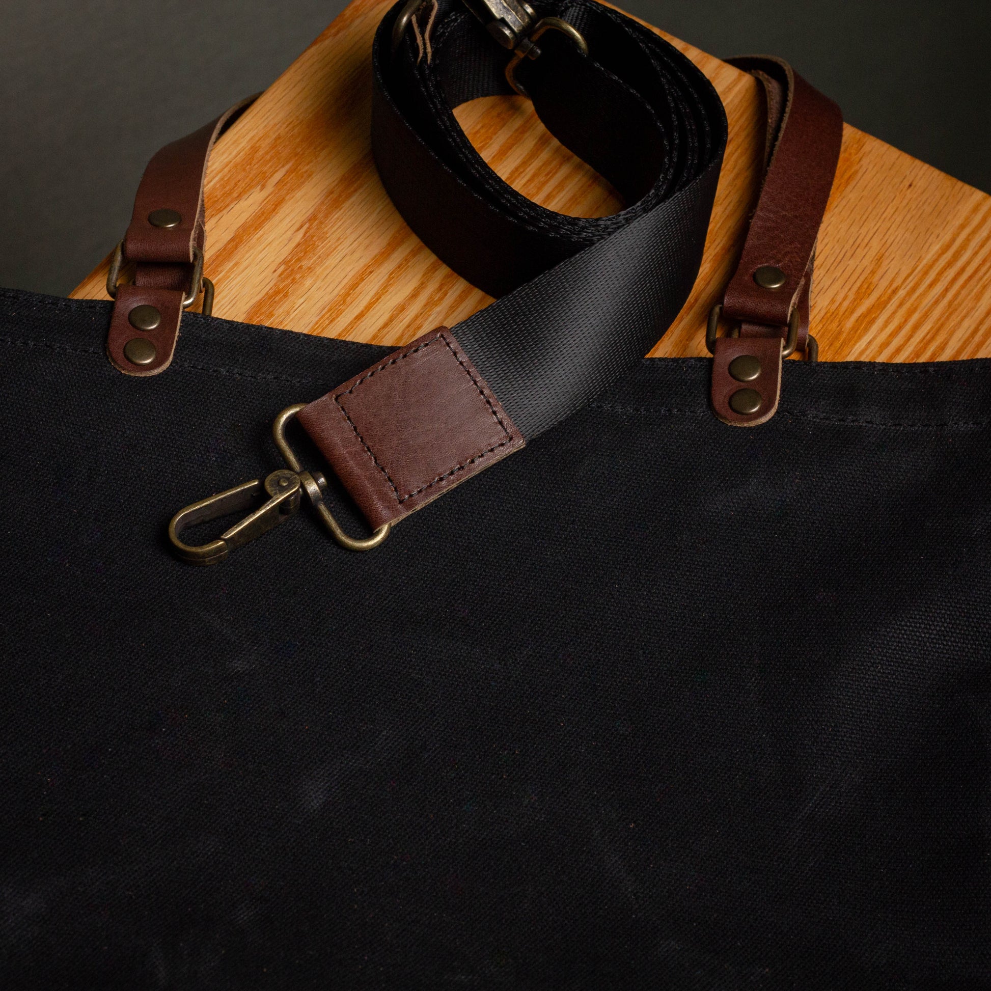 Black and brown leather strap on a black bag with wooden surface underneath