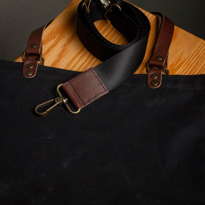 Black and brown leather strap on a black bag with wooden surface underneath