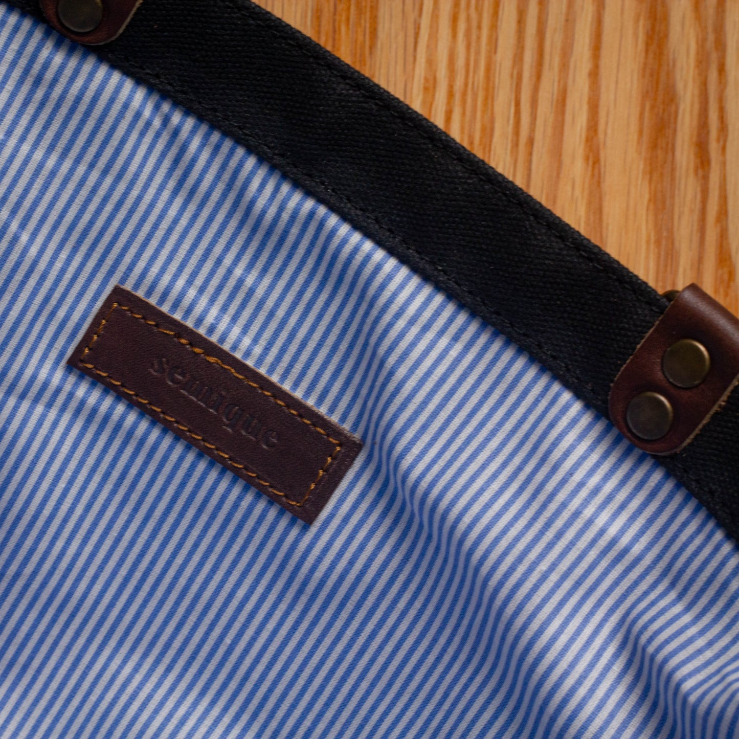 Close-up of a blue and white striped fabric with a leather label and brown buttons on a wooden surface.