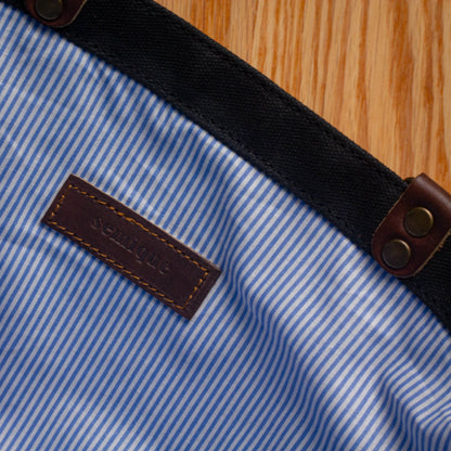 Close-up of a blue and white striped fabric with a leather label and brown buttons on a wooden surface.