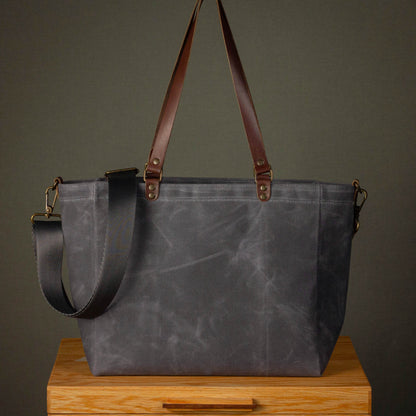 Gray tote bag with brown straps on a wooden surface against a dark background