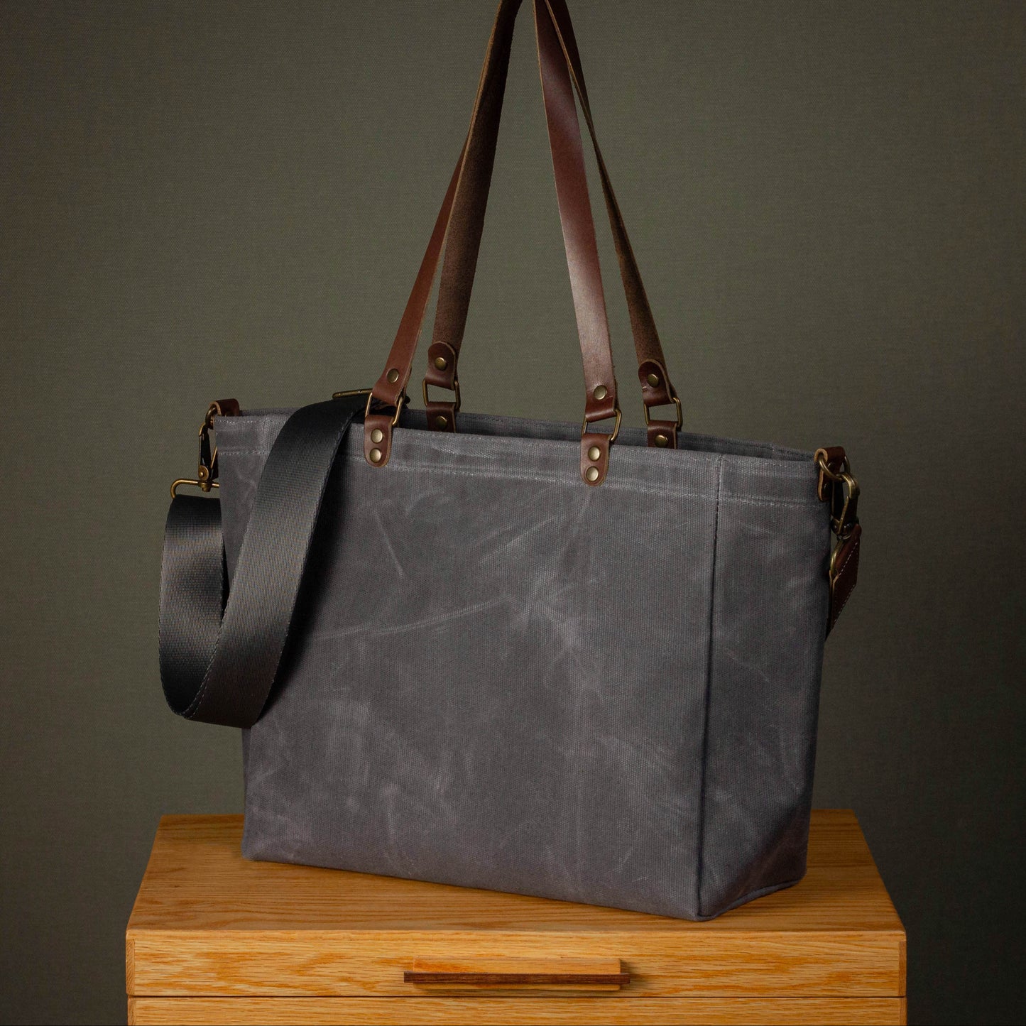 Gray tote bag with brown handles and strap on a wooden surface against a dark background