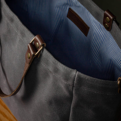 Close-up of a gray bag with leather straps and a blue interior.