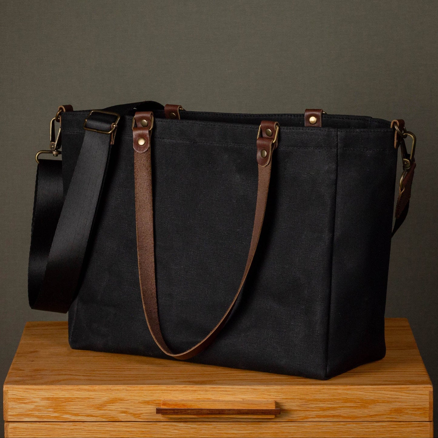 Black tote bag with brown straps on a wooden surface against a gray background