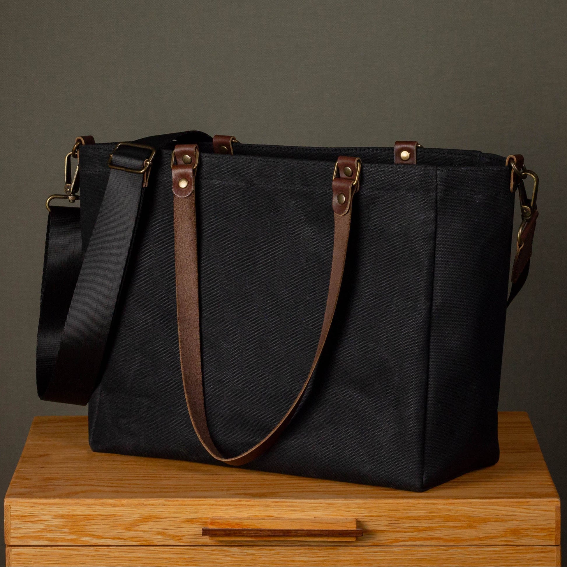 Black tote bag with brown straps on a wooden surface against a gray background