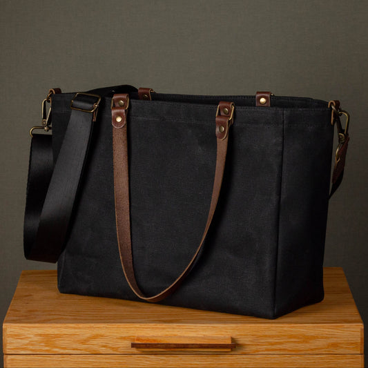 Black tote bag with brown straps on a wooden surface against a gray background