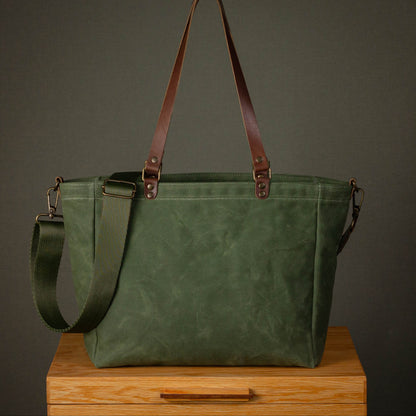 Green tote bag with brown straps on a wooden surface against a dark background