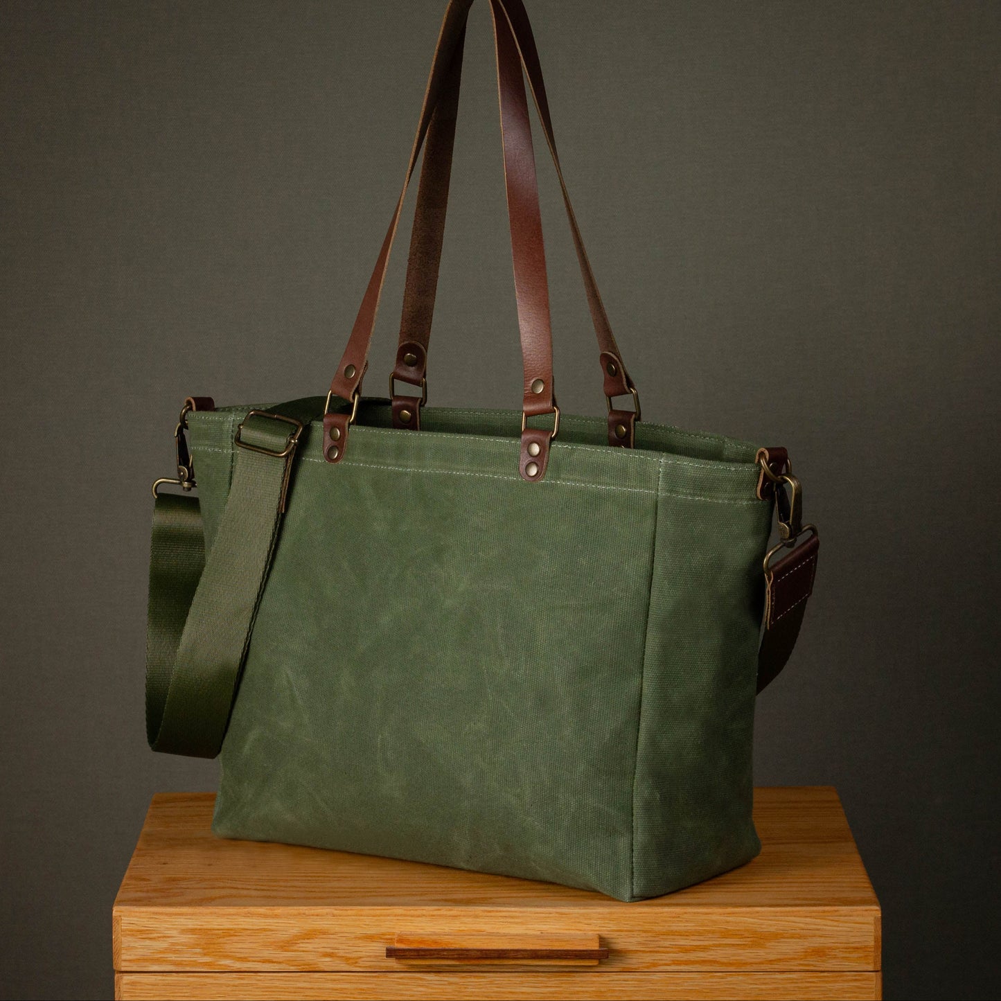 Green tote bag with brown straps on a wooden surface against a gray background