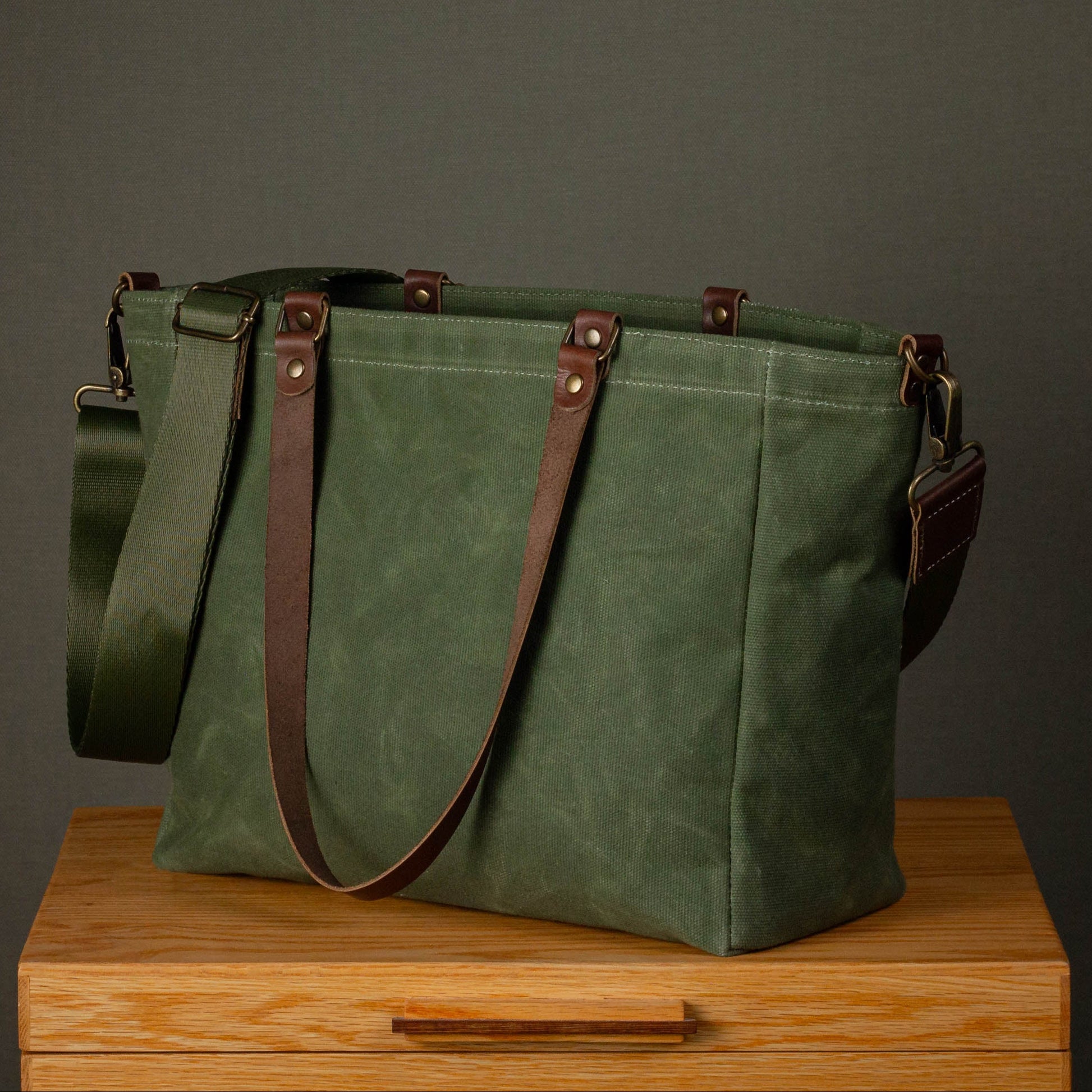 Green canvas bag with brown straps on a wooden surface against a gray background