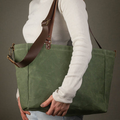 Person holding a green tote bag with a brown strap against a gray background