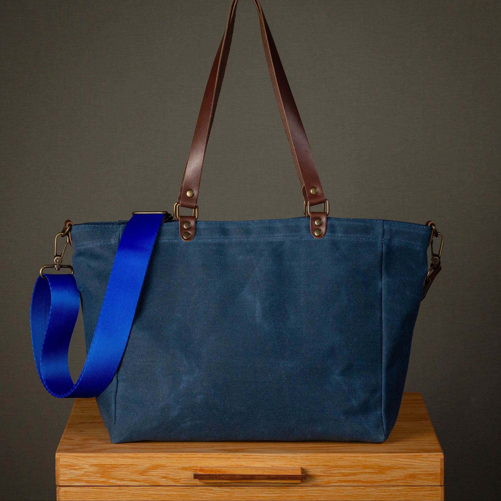 Blue tote bag with brown straps on a wooden surface against a gray background
