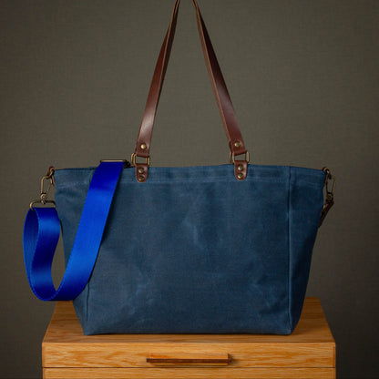 Blue tote bag with brown straps on a wooden surface against a gray background