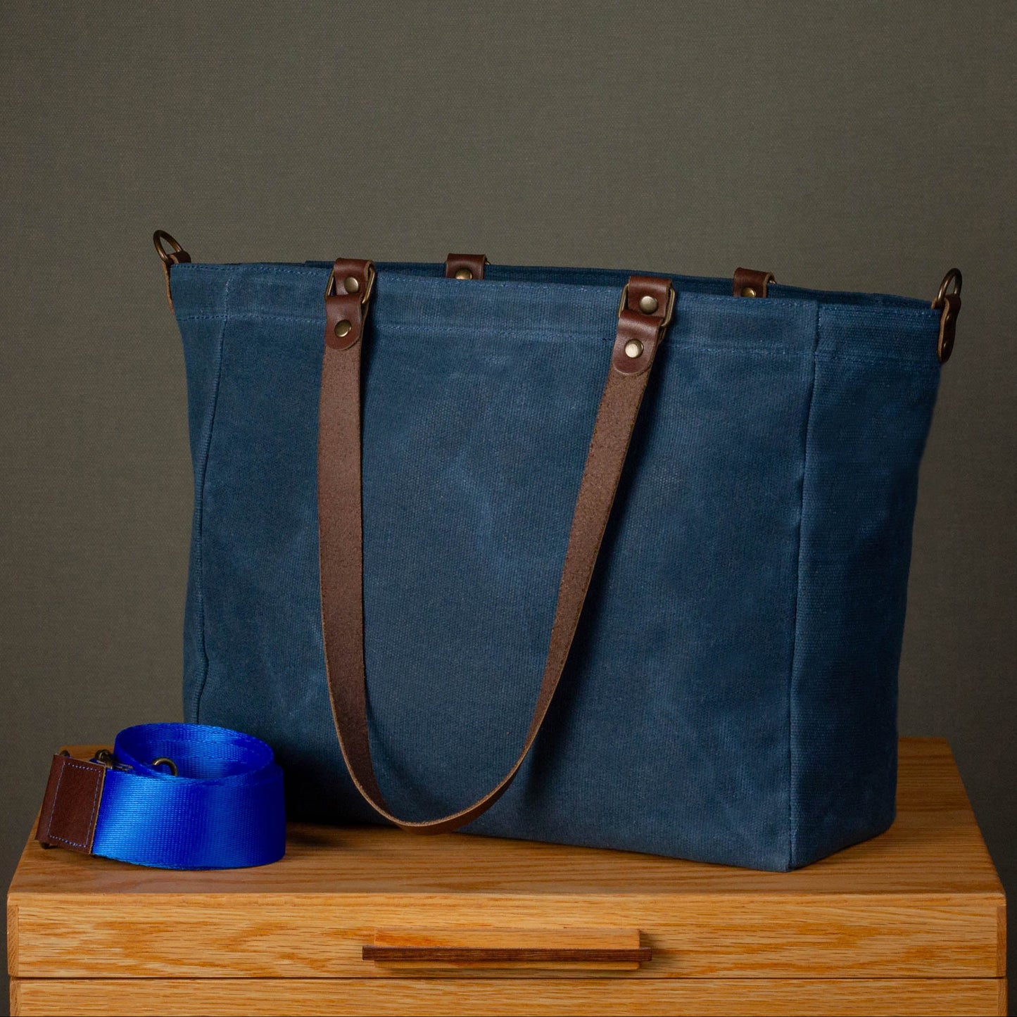Blue tote bag with brown straps on a wooden surface against a gray background