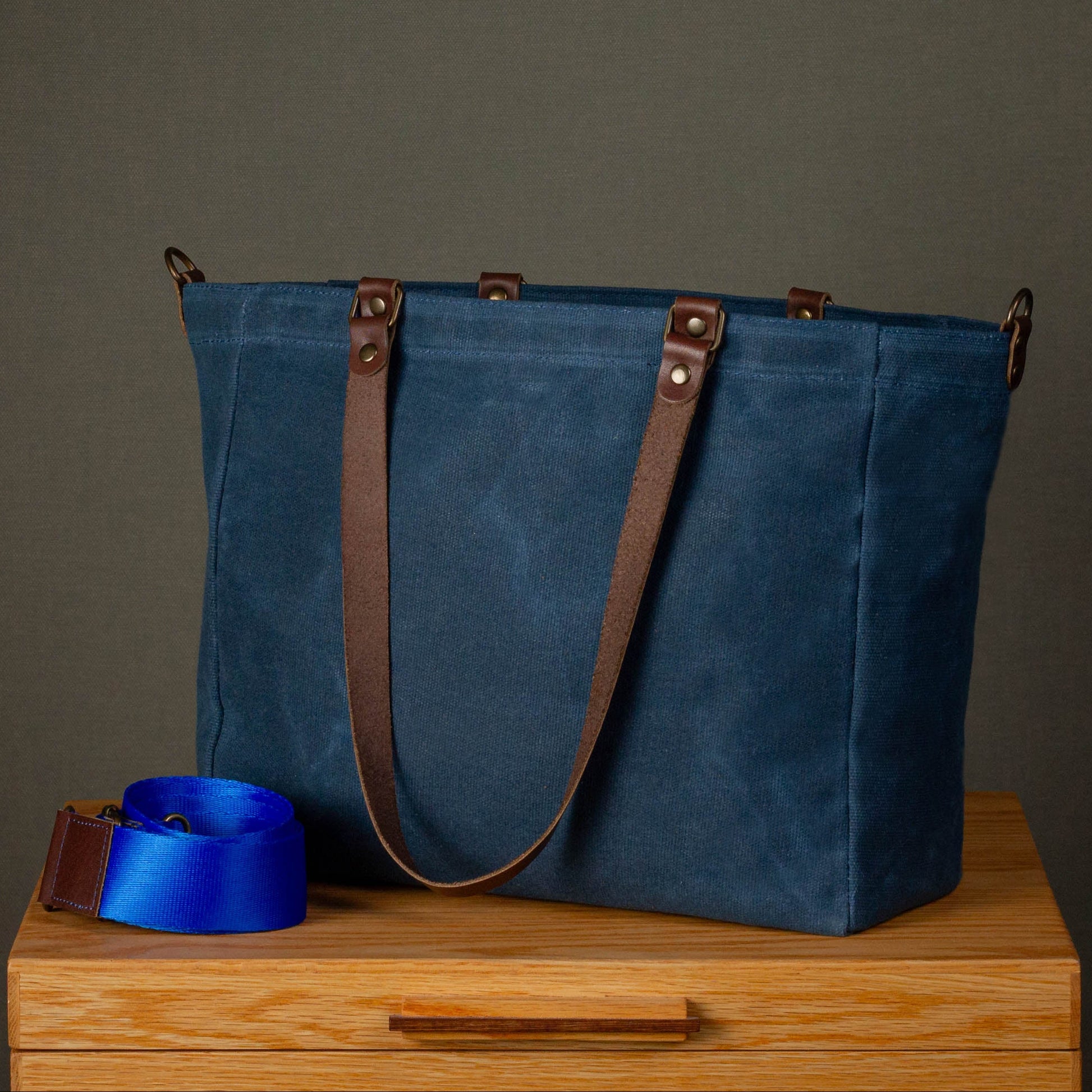 Blue tote bag with brown straps on a wooden surface against a gray background