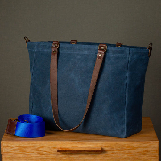 Blue tote bag with brown straps on a wooden surface against a gray background