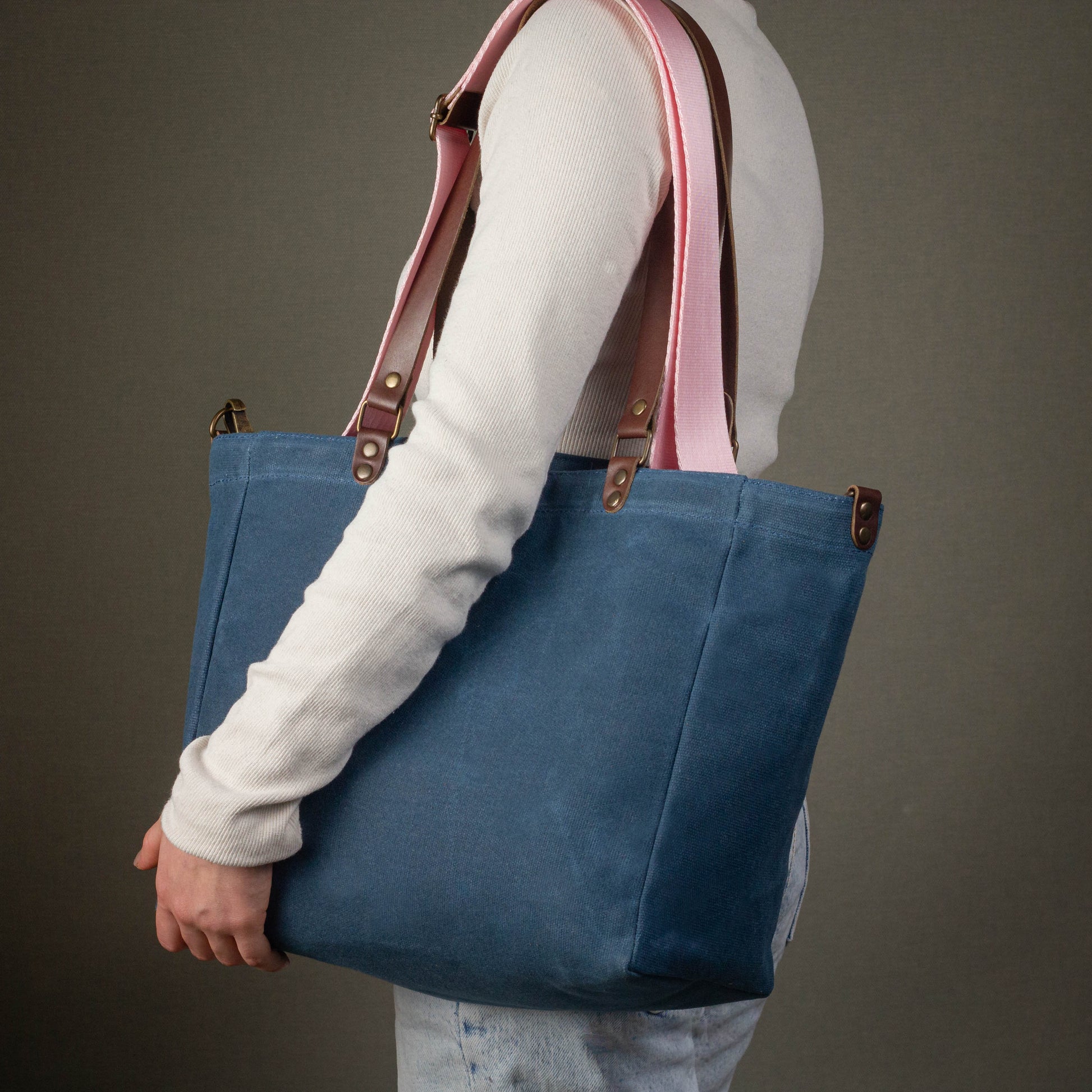 Person holding a blue tote bag with pink straps against a gray background