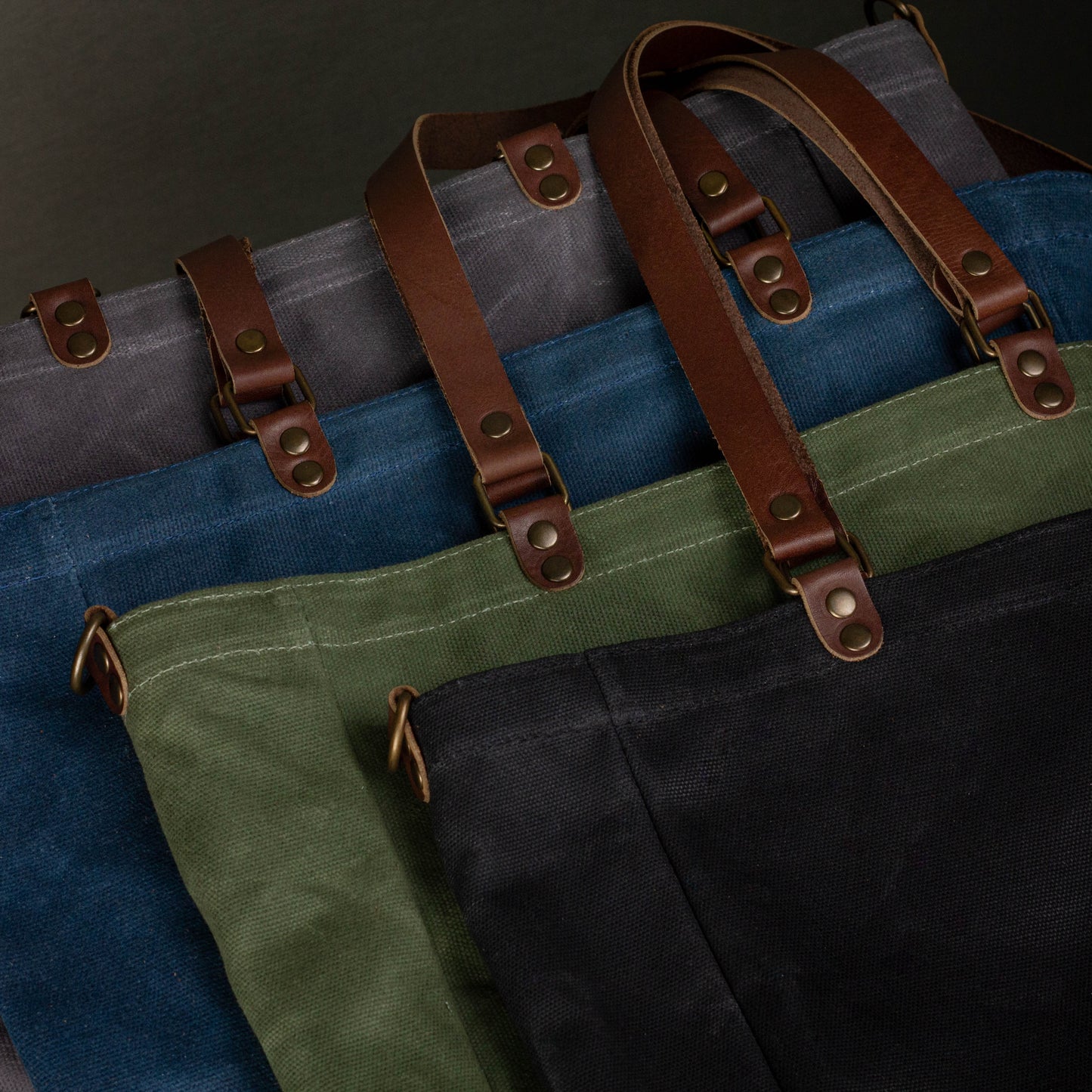 Four bags in gray, blue, green, and black with brown straps on a dark background